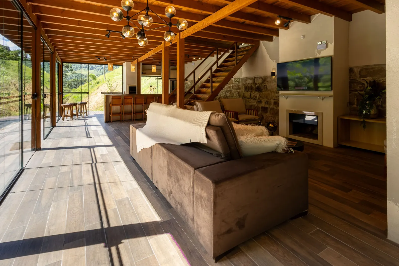 Sala com sofás, lareira e janelas para a mata