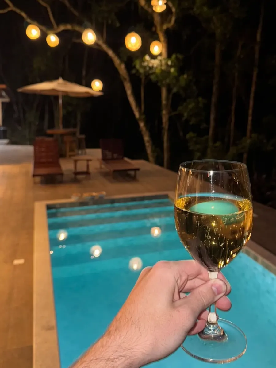 Piscina iluminada à noite com taça de vinho